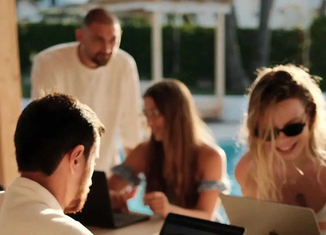 A group of people working on laptops by a pool in a sunny setting.